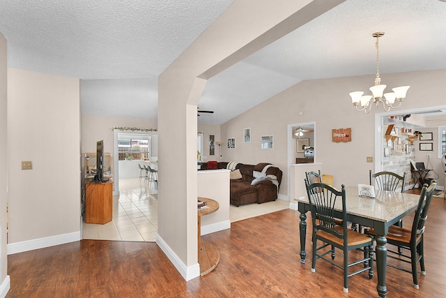 dining area with wood finished floors, baseboards, ceiling fan with notable chandelier, a textured ceiling, and vaulted ceiling