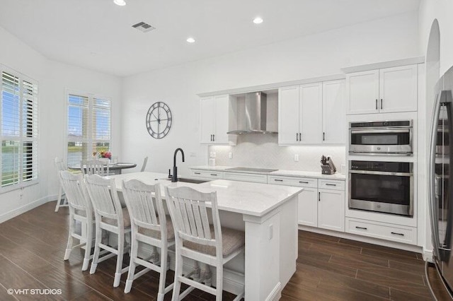 kitchen with sink, wall chimney exhaust hood, white cabinets, and an island with sink