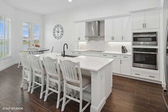 kitchen with sink, white cabinetry, wall chimney exhaust hood, and an island with sink