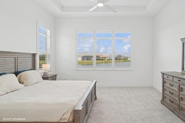 bedroom featuring ceiling fan, multiple windows, a tray ceiling, and light carpet