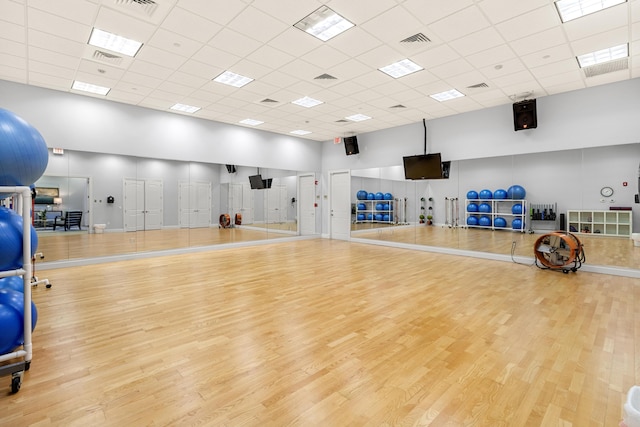 workout area with light hardwood / wood-style flooring, a towering ceiling, and a paneled ceiling