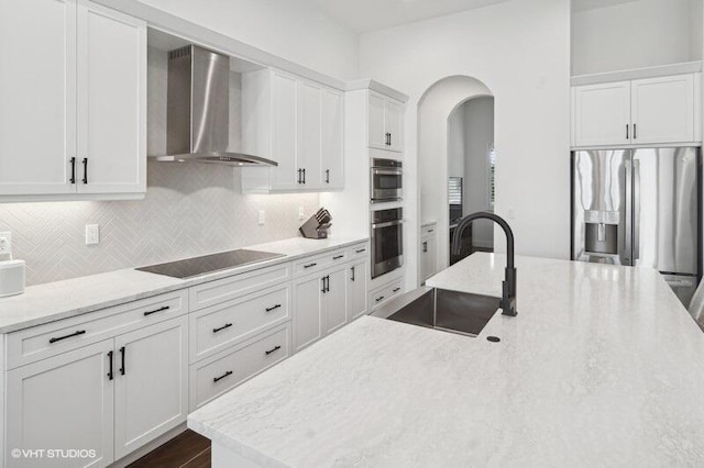 kitchen with sink, white cabinetry, stainless steel appliances, wall chimney exhaust hood, and light stone counters