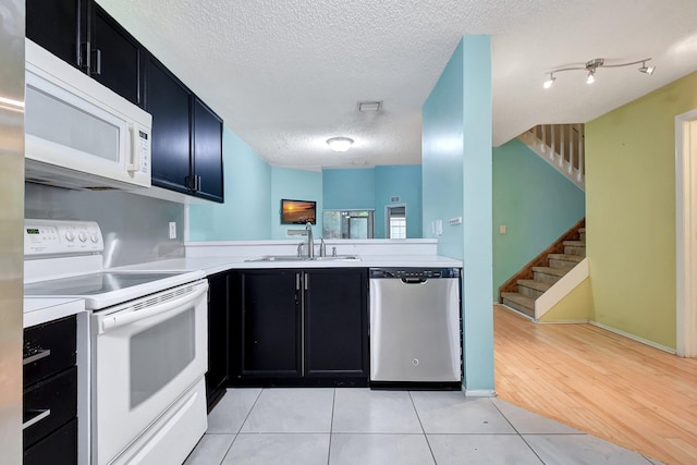 kitchen with kitchen peninsula, sink, white appliances, a textured ceiling, and light tile patterned floors