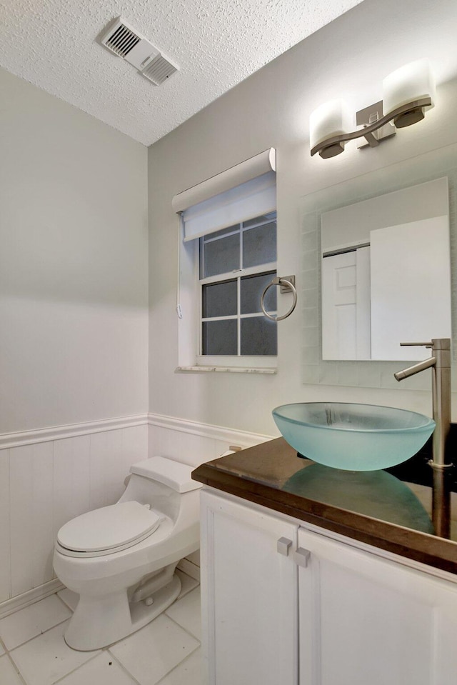 bathroom with a textured ceiling, toilet, tile patterned flooring, and vanity