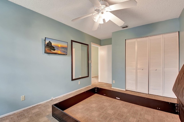 unfurnished bedroom with a textured ceiling, ceiling fan, carpet flooring, and a closet