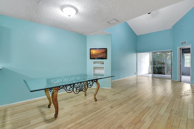 dining area featuring a textured ceiling, lofted ceiling, and light hardwood / wood-style floors