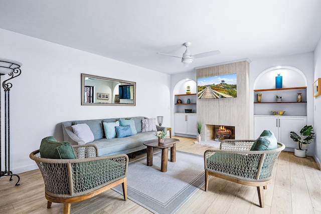 living room featuring ceiling fan, light wood-type flooring, and a large fireplace