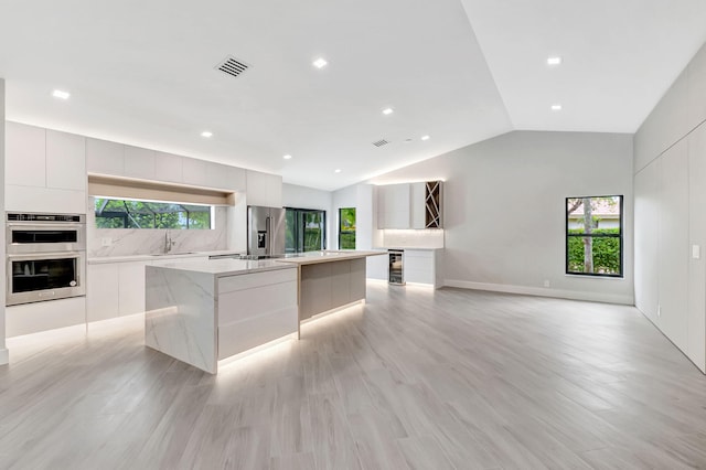 kitchen with lofted ceiling, a large island with sink, sink, appliances with stainless steel finishes, and plenty of natural light