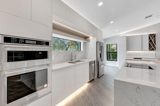 kitchen with white cabinetry, appliances with stainless steel finishes, light stone countertops, vaulted ceiling, and sink