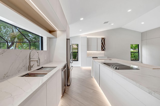 kitchen featuring stainless steel appliances, lofted ceiling, light stone counters, and sink