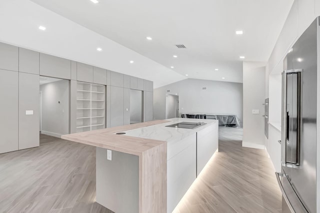 kitchen featuring lofted ceiling, gray cabinets, a spacious island, high quality fridge, and light stone countertops