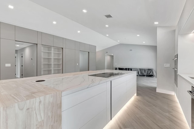 kitchen with lofted ceiling, black electric stovetop, light hardwood / wood-style floors, double oven, and light stone counters