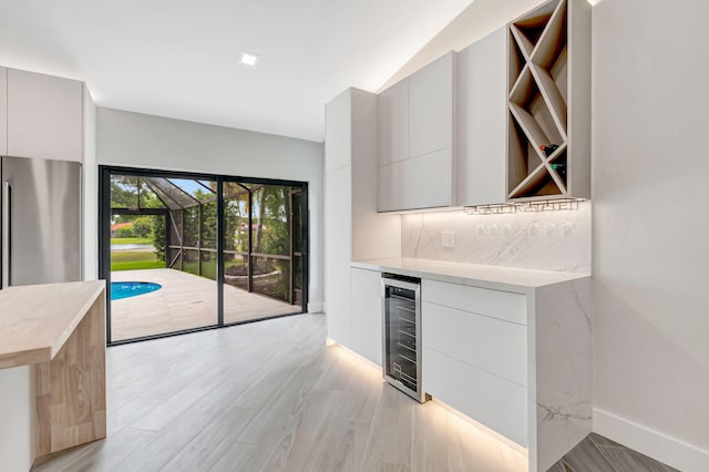 kitchen featuring white cabinets, lofted ceiling, wine cooler, decorative backsplash, and stainless steel refrigerator