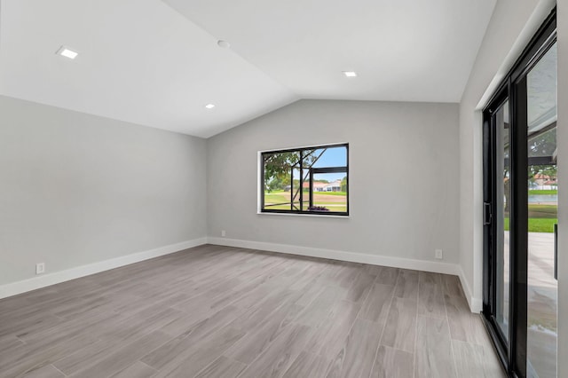 spare room with light wood-type flooring and lofted ceiling