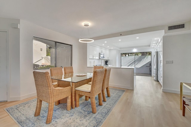 dining area featuring plenty of natural light, sink, light wood-type flooring, and a tray ceiling