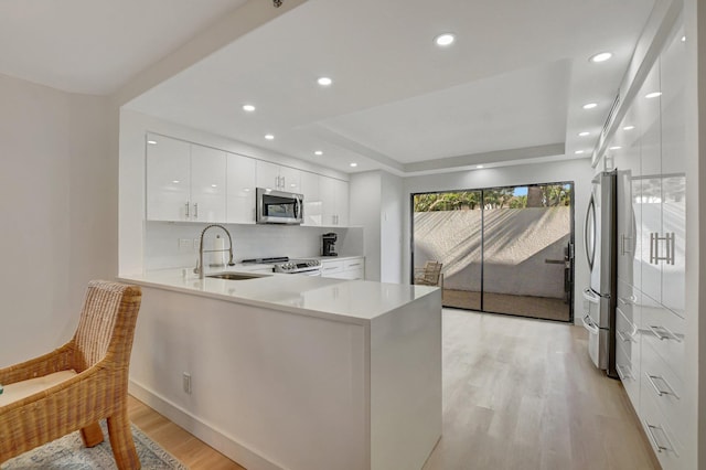 kitchen with sink, appliances with stainless steel finishes, a tray ceiling, white cabinets, and kitchen peninsula