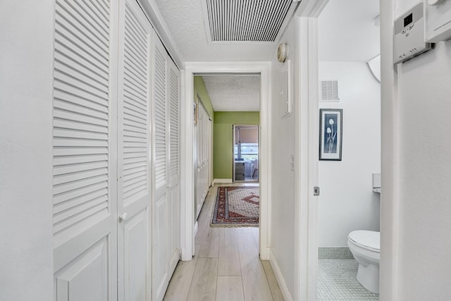 hall with light hardwood / wood-style floors and a textured ceiling