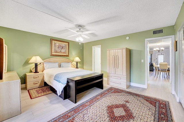 bedroom with light wood-type flooring, ceiling fan with notable chandelier, and a textured ceiling