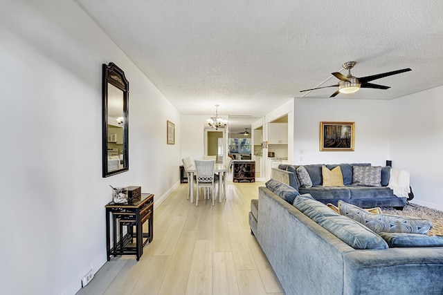 living room featuring light wood-type flooring, ceiling fan with notable chandelier, and a textured ceiling