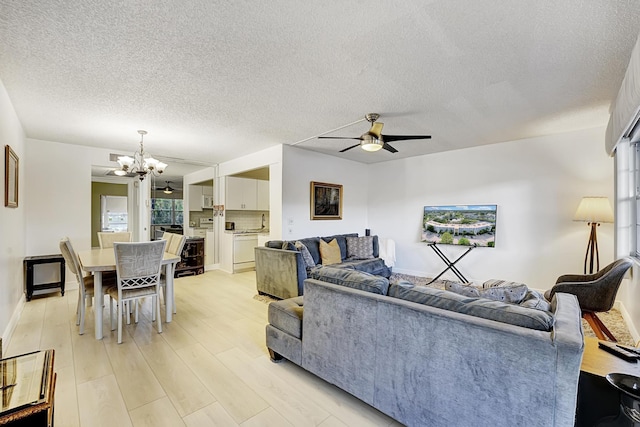 living room with ceiling fan with notable chandelier, light hardwood / wood-style floors, and a textured ceiling