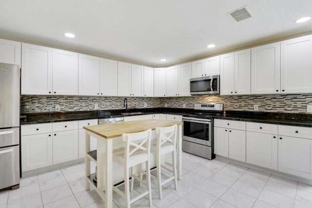 kitchen with white cabinetry, stainless steel appliances, a kitchen bar, and tasteful backsplash