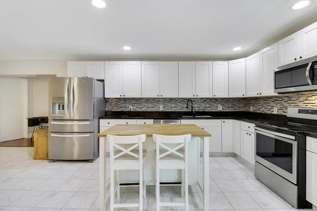 kitchen with sink, a breakfast bar area, white cabinetry, stainless steel appliances, and a kitchen island