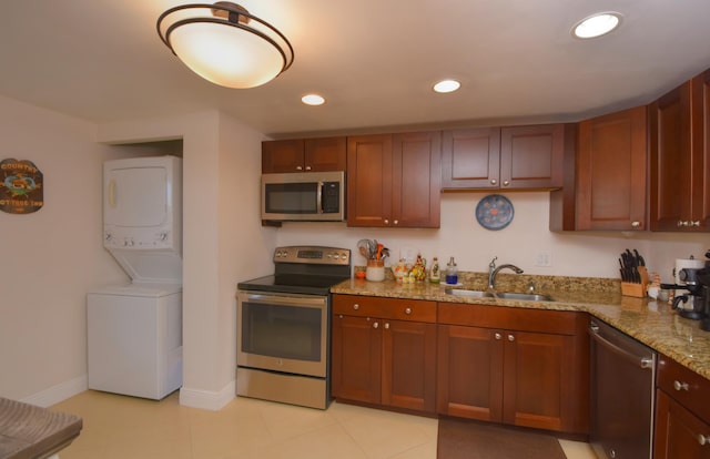 kitchen with stainless steel appliances, light stone countertops, sink, and stacked washer / drying machine