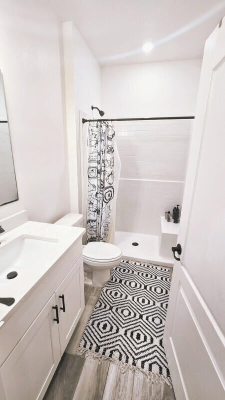 bathroom with hardwood / wood-style flooring, curtained shower, toilet, and vanity