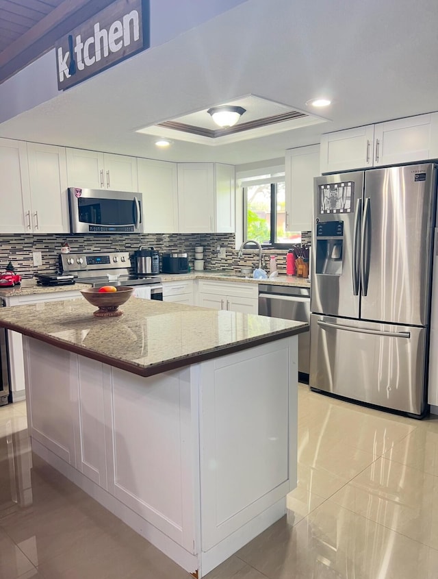 kitchen featuring light stone countertops, white cabinetry, a center island, and stainless steel appliances