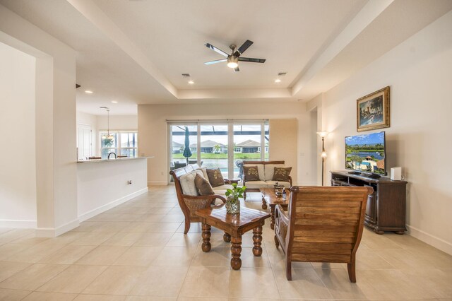 living room with ceiling fan with notable chandelier, plenty of natural light, and a tray ceiling