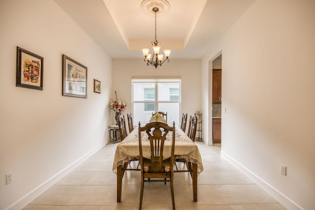 tiled dining area with a raised ceiling and a notable chandelier