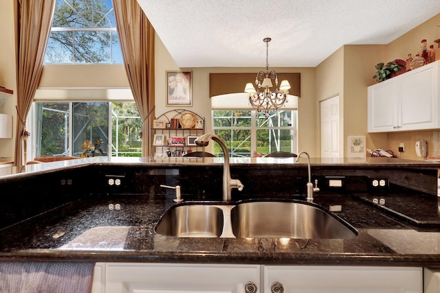 kitchen with pendant lighting, a healthy amount of sunlight, dark stone countertops, and white cabinets