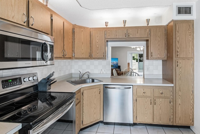 kitchen with sink, backsplash, light tile patterned floors, and appliances with stainless steel finishes