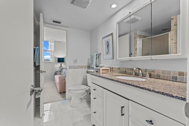 bathroom with toilet, vanity, tile walls, and a shower with shower door