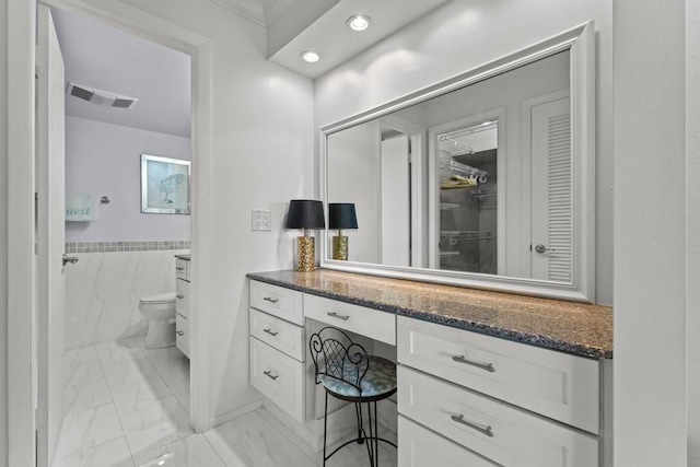 bathroom featuring toilet, vanity, and tile walls