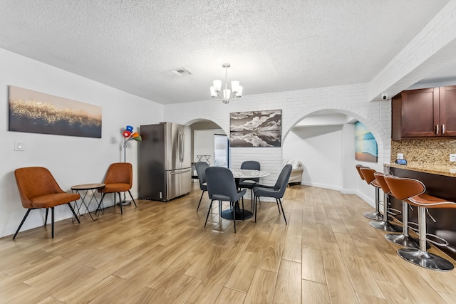 dining room featuring a textured ceiling, an inviting chandelier, brick wall, and light hardwood / wood-style floors