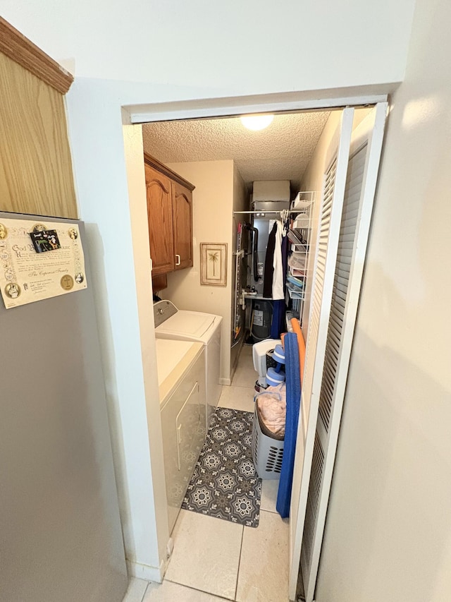 laundry room with cabinets, washer and dryer, a textured ceiling, and light tile patterned floors