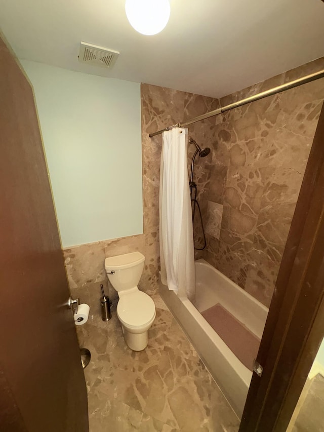 bathroom featuring tile walls, toilet, and shower / tub combo with curtain