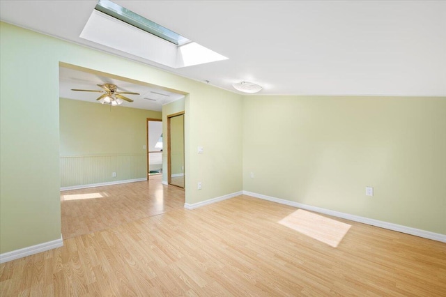 unfurnished room featuring a skylight, ceiling fan, and light hardwood / wood-style flooring