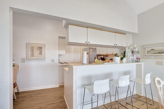 kitchen with stainless steel fridge, a breakfast bar, white cabinetry, kitchen peninsula, and light wood-type flooring