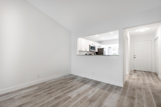 unfurnished living room featuring vaulted ceiling and light hardwood / wood-style floors