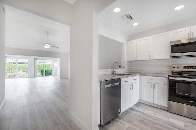 kitchen featuring white cabinetry, stainless steel appliances, tasteful backsplash, light stone counters, and sink