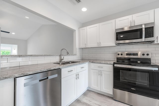 kitchen featuring white cabinetry, stainless steel appliances, backsplash, vaulted ceiling, and sink