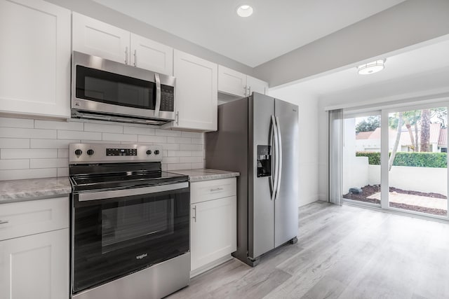 kitchen featuring white cabinets, backsplash, appliances with stainless steel finishes, and light hardwood / wood-style flooring