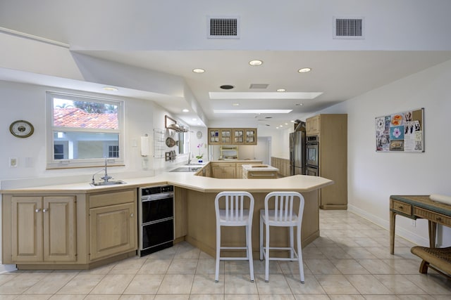 kitchen featuring light tile patterned floors, kitchen peninsula, a breakfast bar area, oven, and sink