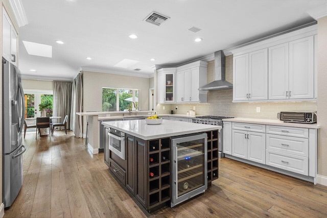 kitchen with a kitchen island, appliances with stainless steel finishes, white cabinetry, beverage cooler, and wall chimney exhaust hood