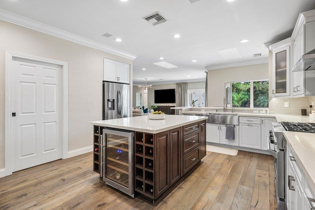 kitchen with stainless steel appliances, wine cooler, dark brown cabinetry, a kitchen island, and light wood-type flooring