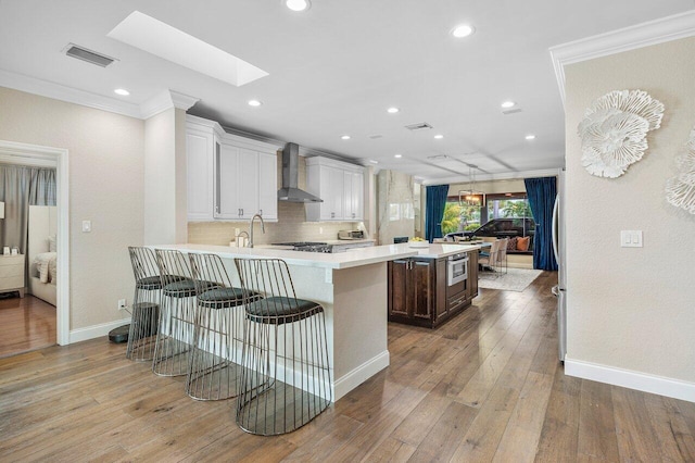 kitchen with wall chimney range hood, a breakfast bar, a skylight, white cabinets, and kitchen peninsula