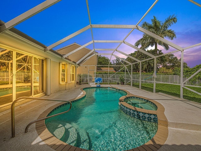 pool at dusk featuring glass enclosure, a patio area, and an in ground hot tub