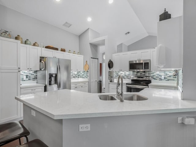 kitchen with white cabinetry, stainless steel appliances, sink, vaulted ceiling, and a breakfast bar area